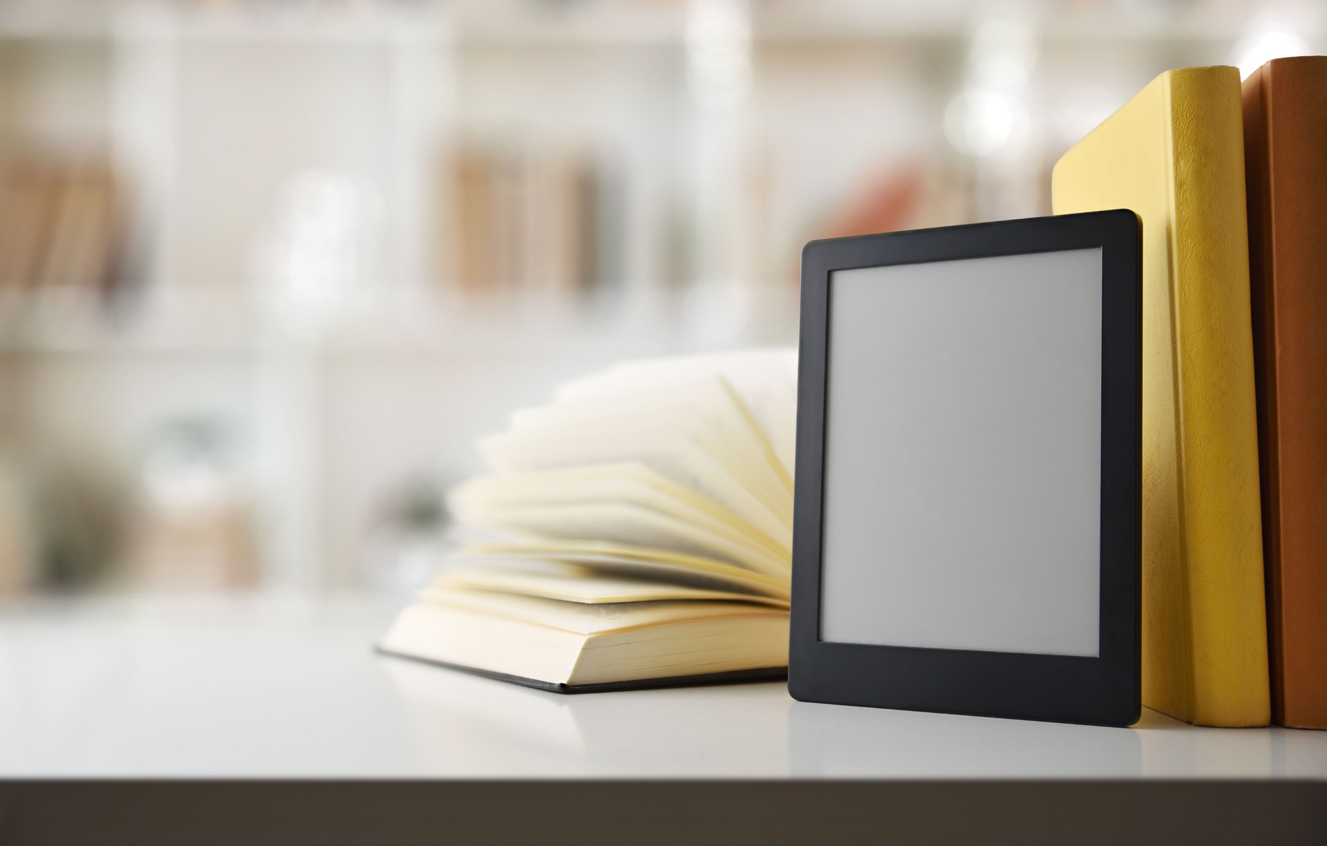 Digital reading concept with ebook on gray bookshelf with traditional paper books and bookshelf full of books in the background.